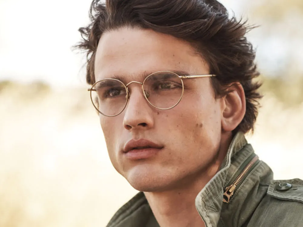 Man wearing round gold metal glasses frames outdoors.
