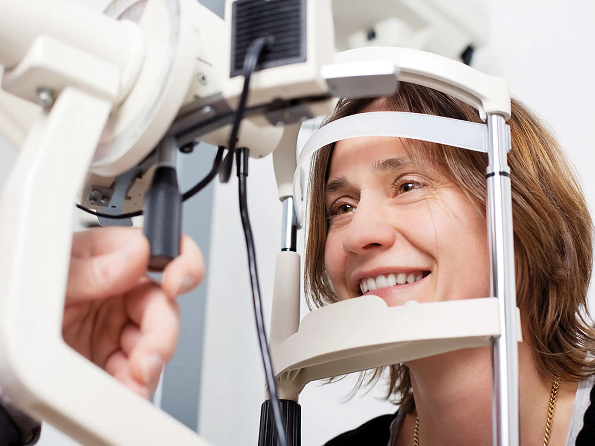 Smiling patient resting her chin on a slit lamp while having her eyes examined.