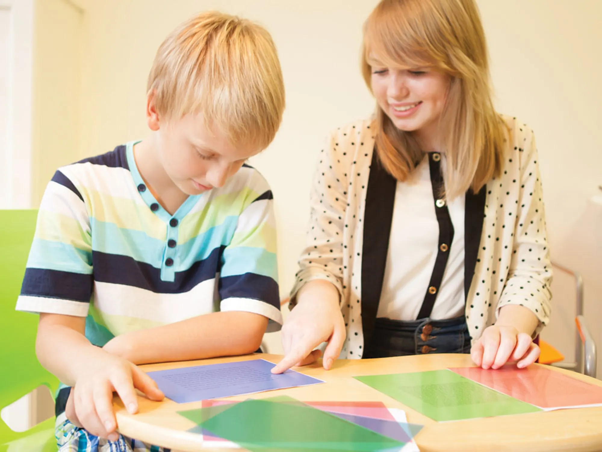 Practitioner helping a boy read text through a coloured overlay during a visual stress assessment.