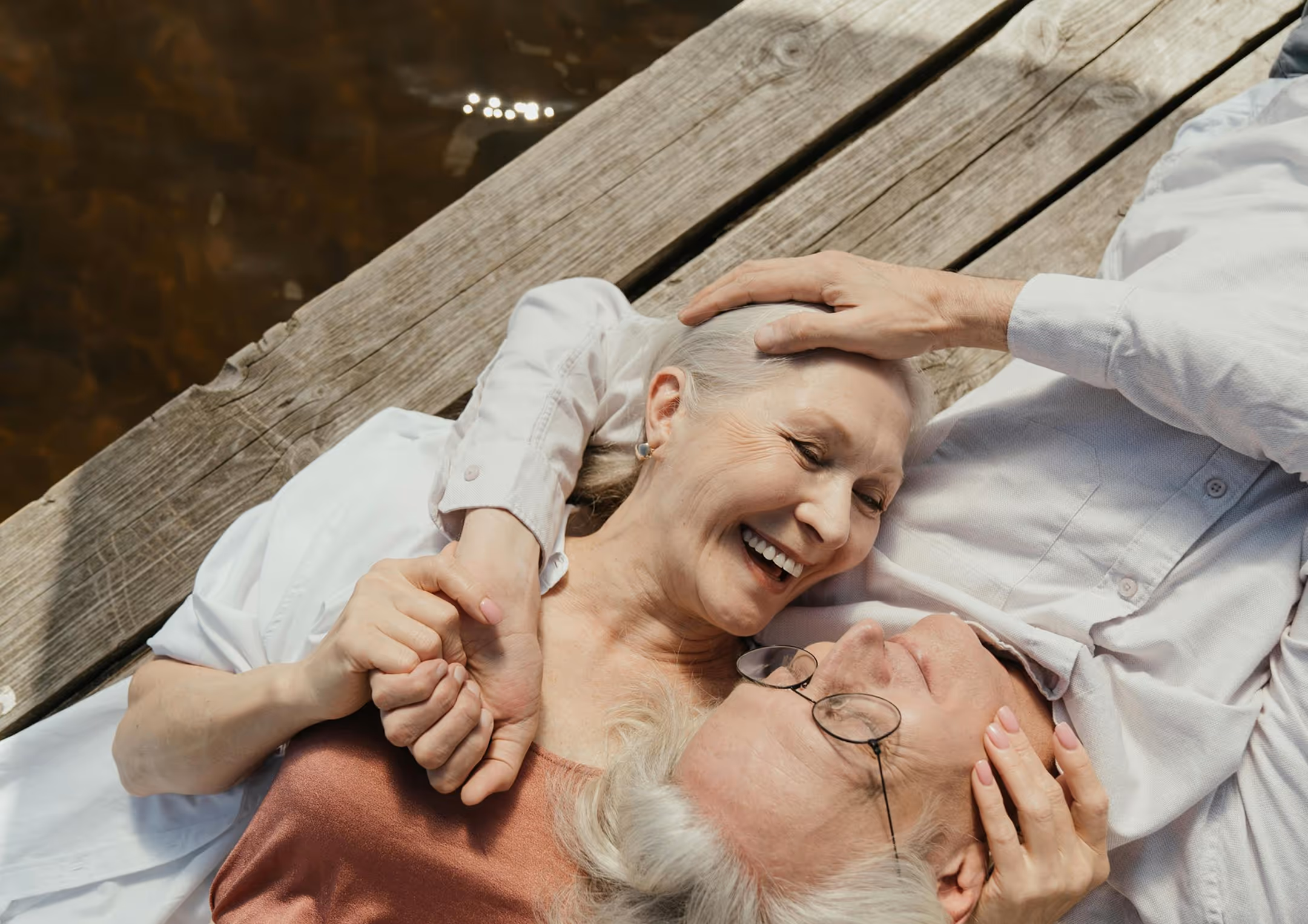 Smiling elderly couple touching foreheads outdoors on a sunny day.
