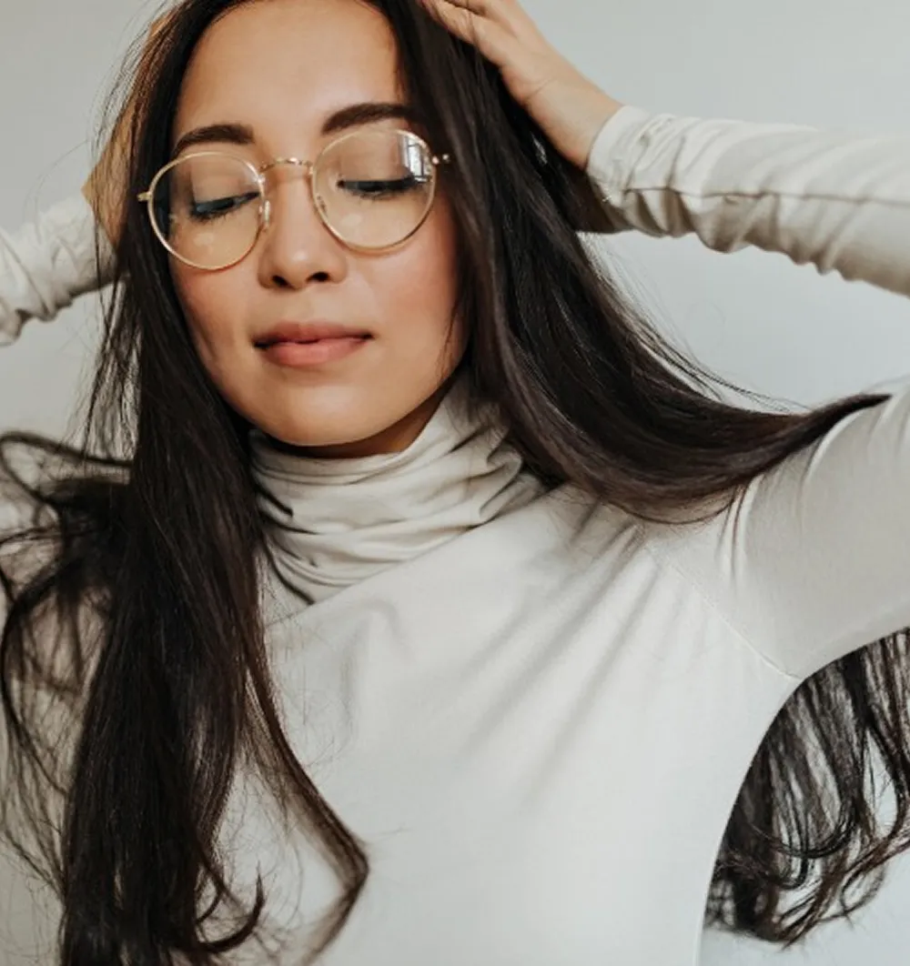 Woman with long dark hair wearing round glasses and a white turtleneck with eyes closed.