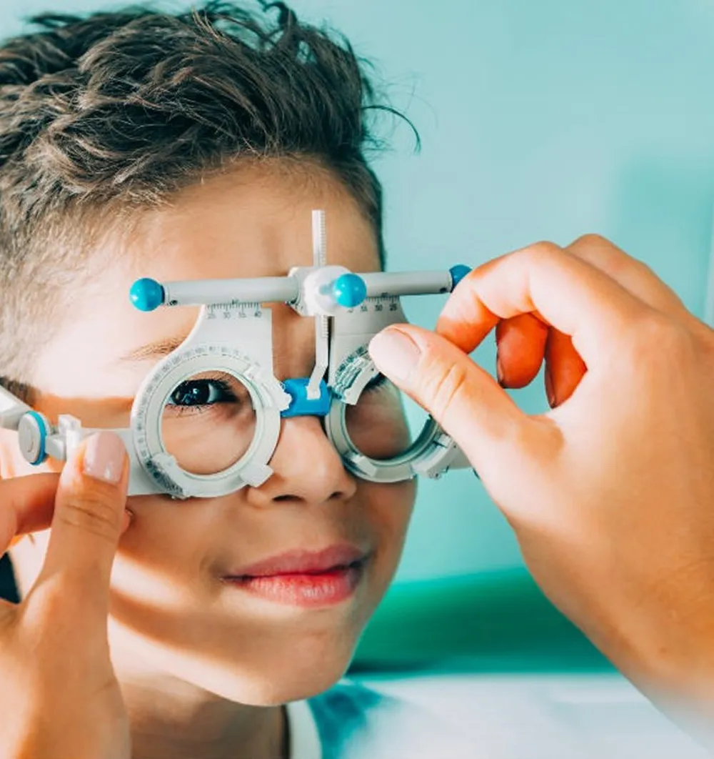 Child having eyes tested with a trial frame adjusted by an optometrist's hands.