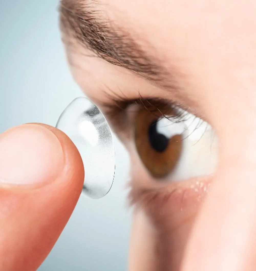 Close-up of a finger holding a contact lens near a brown eye.
