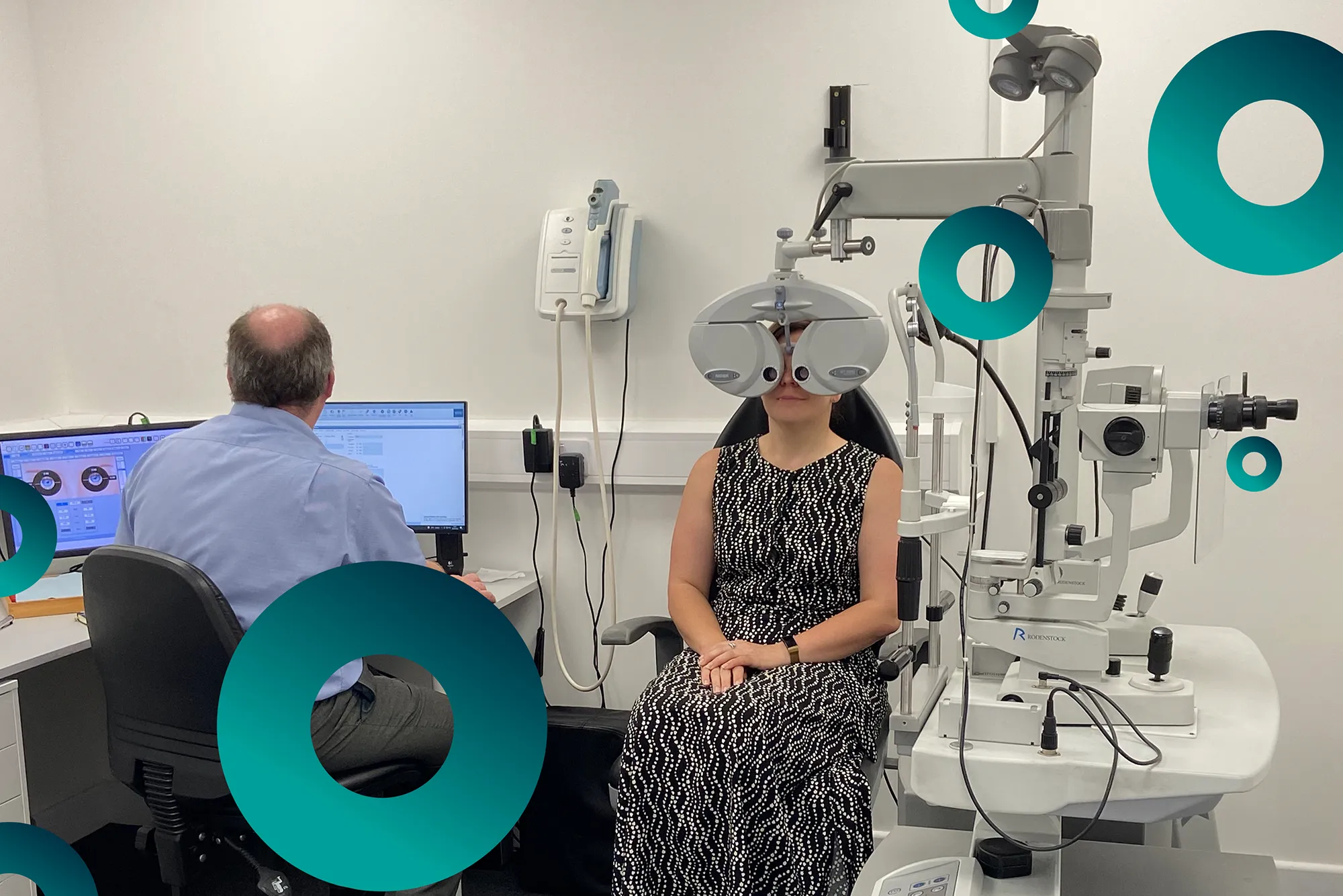 Woman undergoing eye exam with phoropter while an optometrist reviews results on computer.
