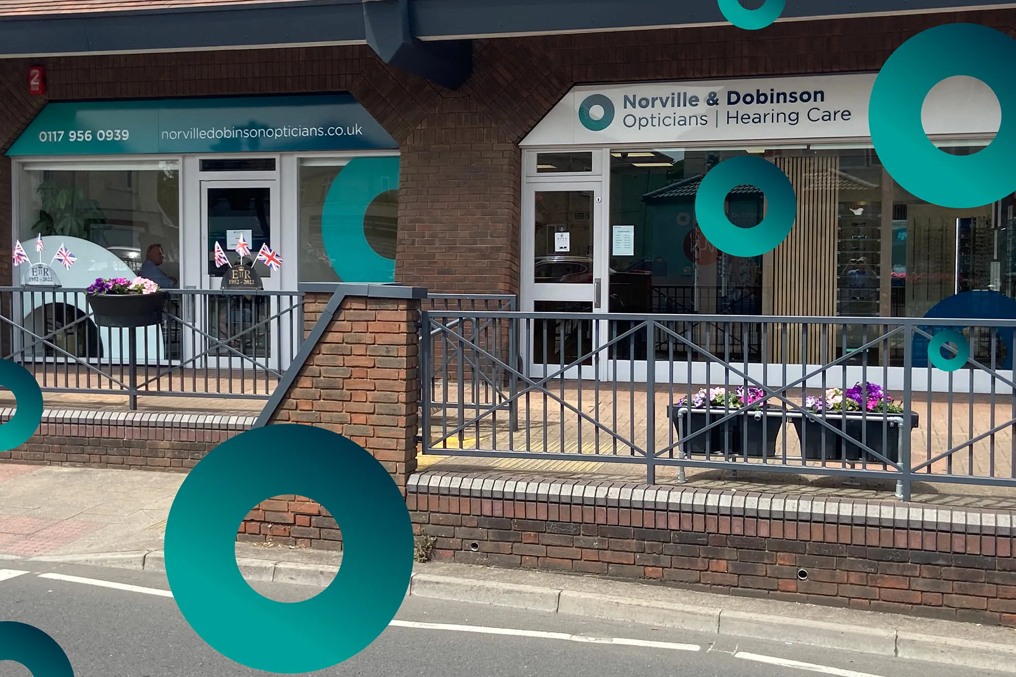 Storefront of Norville & Dobinson Opticians and Hearing Care with UK flags and flower pots outside.