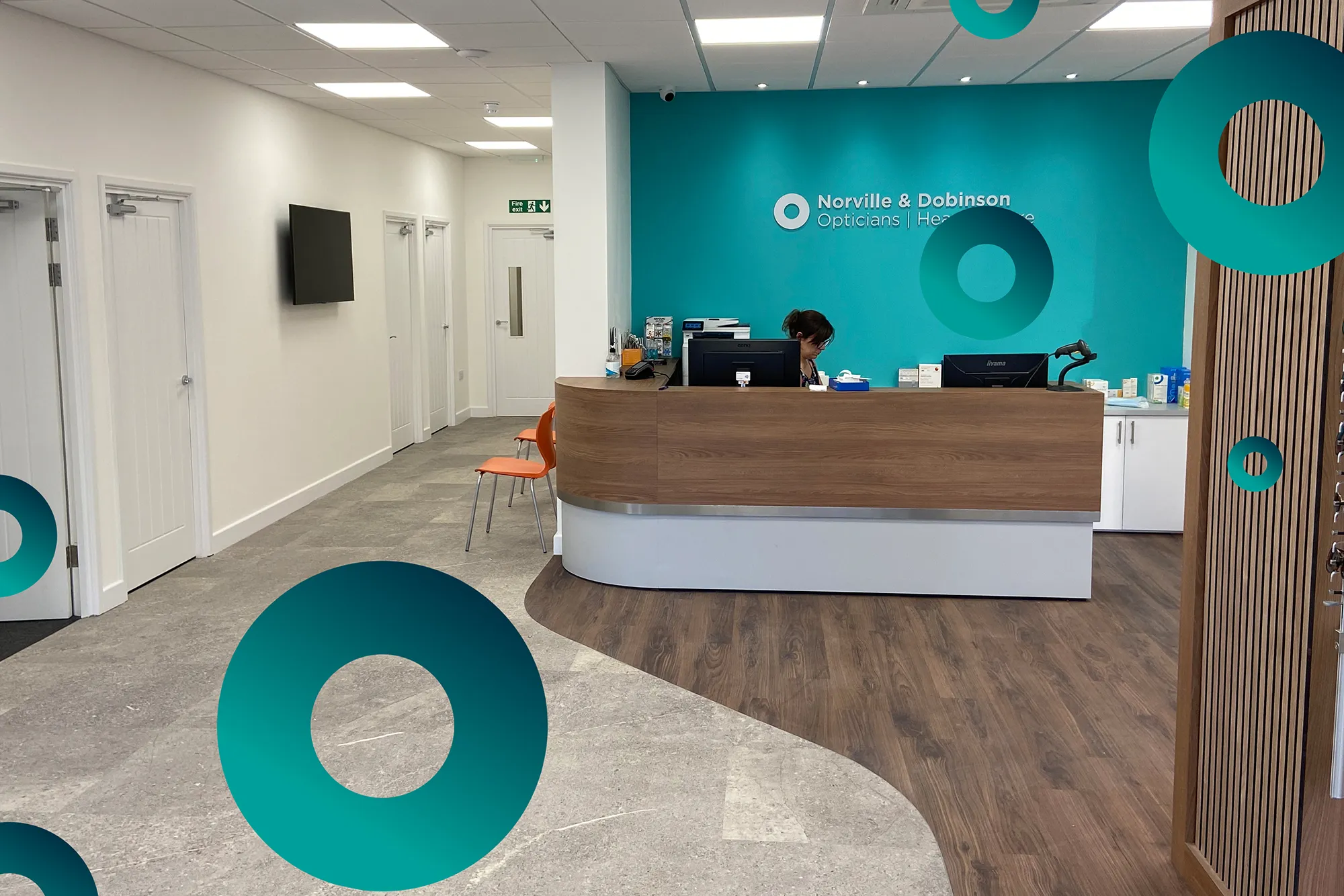 Reception desk with staff working inside Norville & Dobinson Opticians with blue accent wall.
