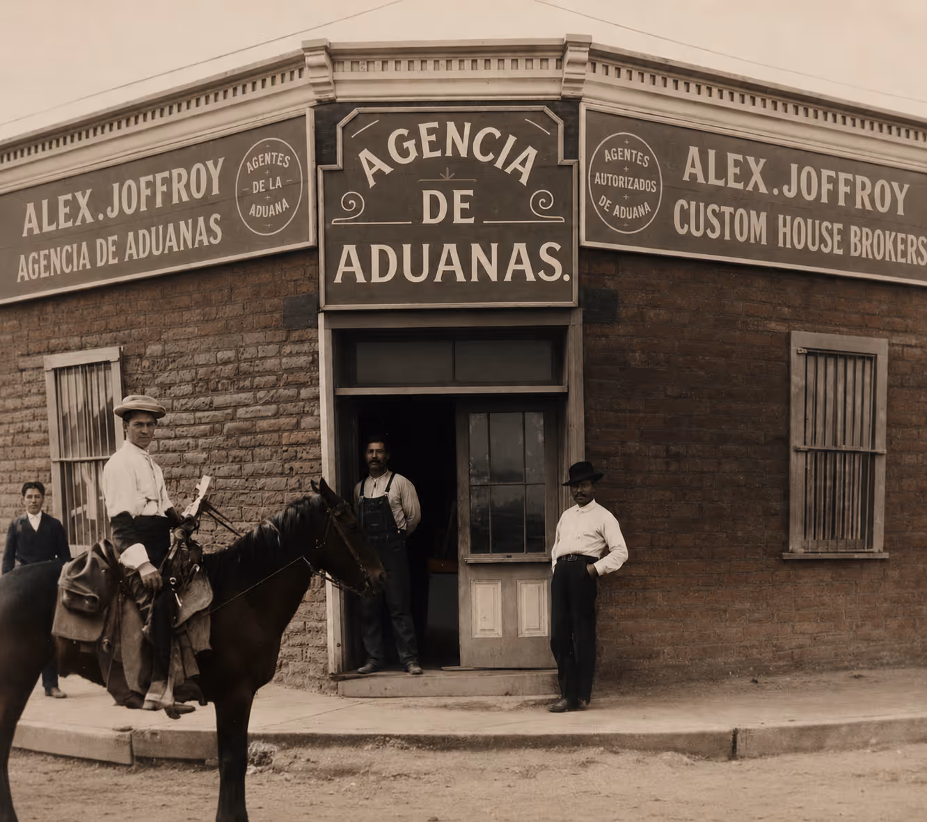 Four men near a brick building with signs for Alex Joffroy Customs and Agencia de Aduanas.