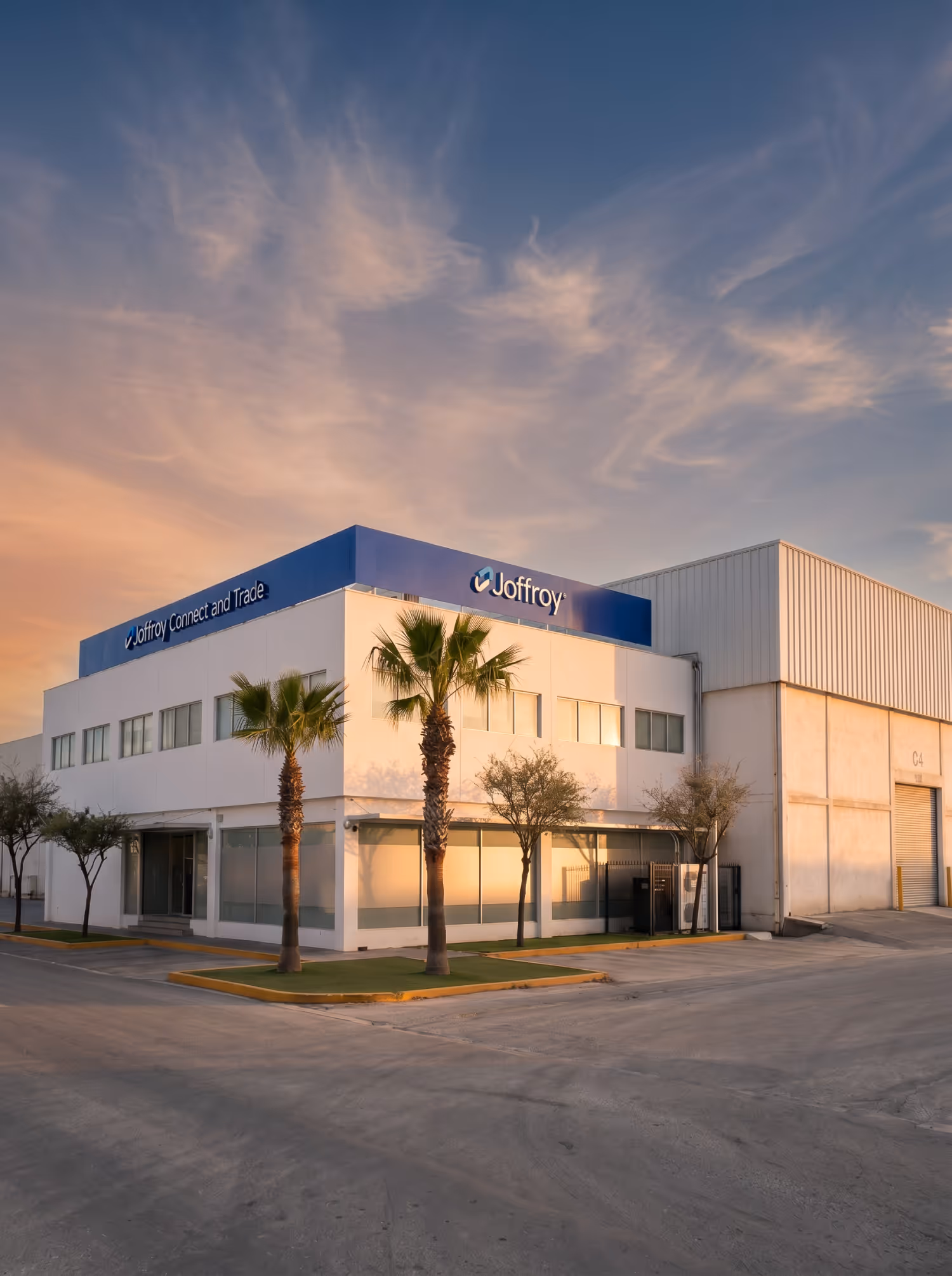 Modern white commercial building with blue Joffroy signage and palm trees at sunset.