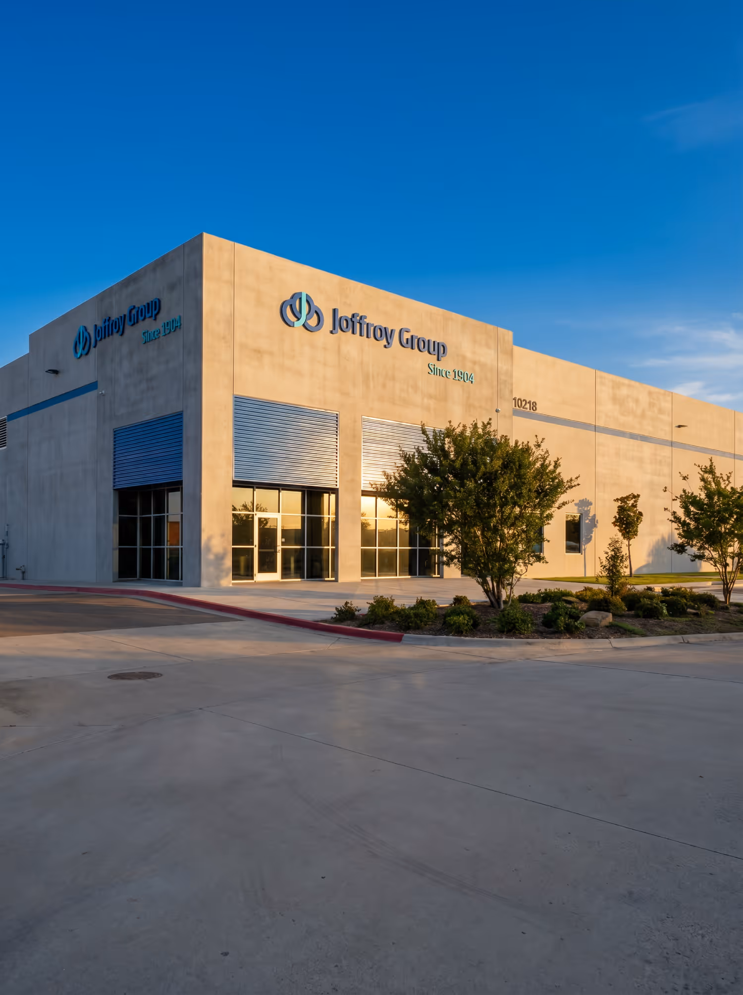 Joffroy Group building with logo, windows, and trees under clear blue sky during sunset.