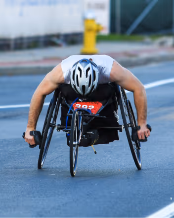 Athlete in a wheelchair pushing forward on an outdoor road race.