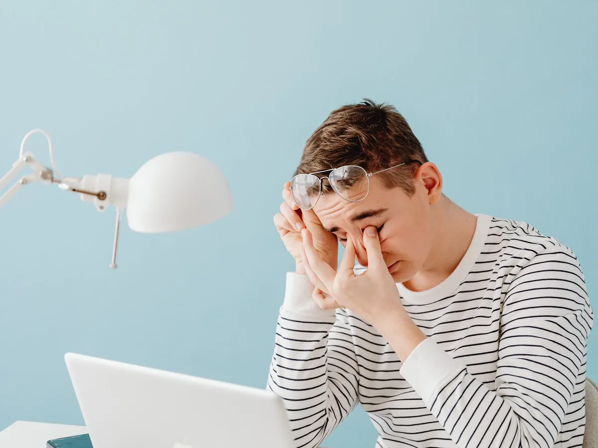 Man at a laptop pressing the bridge of his nose with his glasses pushed up, a sign of digital eye strain