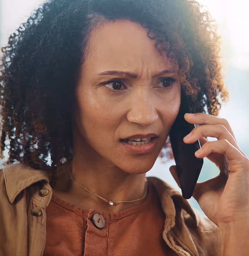 Concerned woman with curly hair speaking on a smartphone.