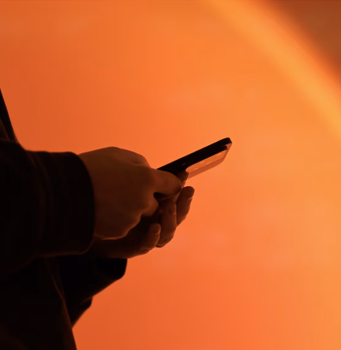 Person holding and using a smartphone with an orange blurred background.