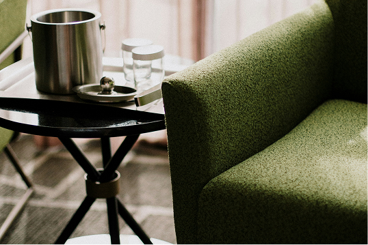 Close-up of a green upholstered armchair next to a small black side table with a silver ice bucket and two empty glass jars.