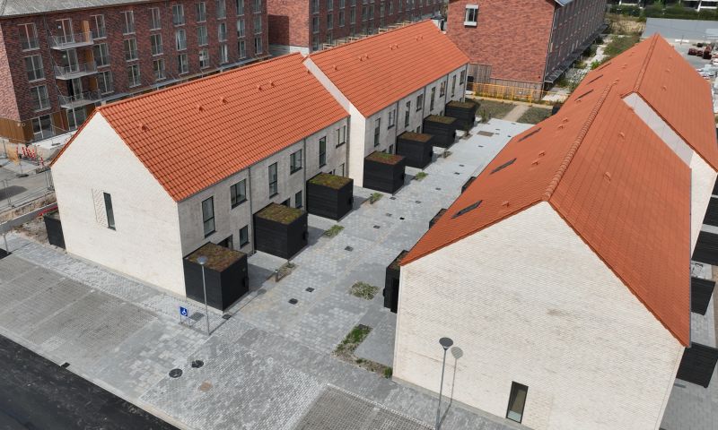 Aerial view of two rows of modern white brick townhouses with orange tiled roofs and small black patios facing a gray paved courtyard.
