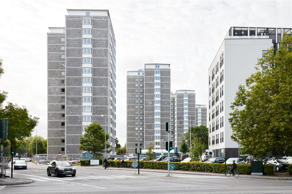 Modern residential high-rise buildings along a street with cars, cyclists, and green trees on both sides.