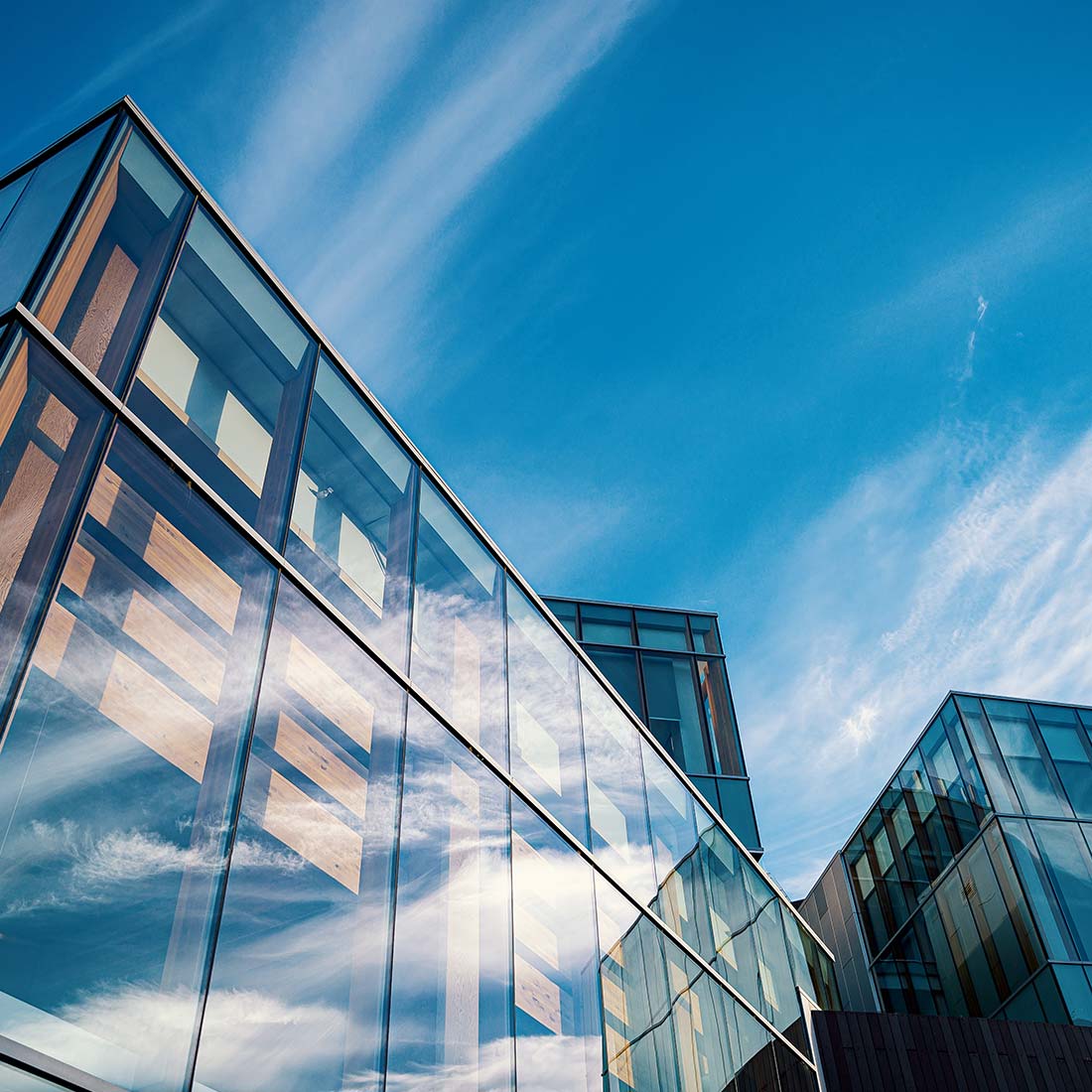 Modern glass building reflecting a blue sky with wispy clouds.