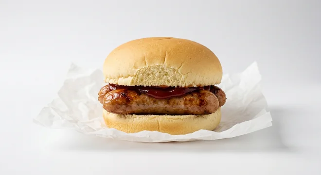 LEON Sausage Muffin with Gluten-Free Bun, gluten-free bun with a Cumberland sausage and ketchup on white paper, nutrition and calories