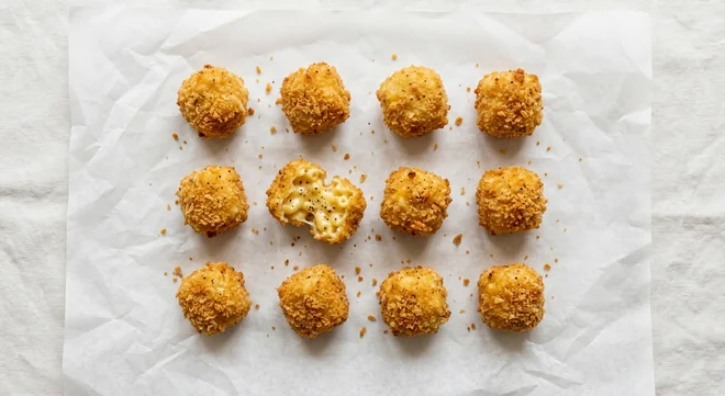 LEON Cheddar and Black Pepper Mac Bites (12), twelve breaded cheddar mac and cheese bites, one broken open on white paper, nutrition and calories