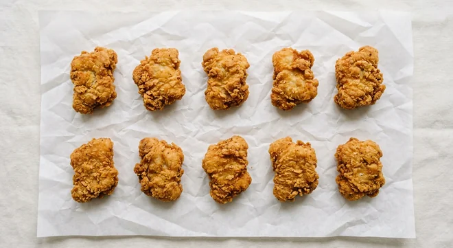 LEON GFC Crispy Chicken Nuggets (10 Pieces), ten crispy gluten-free chicken thigh nuggets on white paper, nutrition and calories