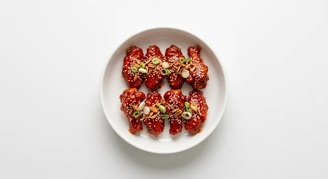 Wagamama Buldak Fire Wings, eight chicken wings in fiery red buldak sauce with crispy onions, spring onion and sesame seeds in a white bowl, nutrition and calories