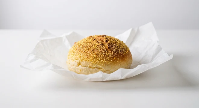 Greggs Corn Topped Roll, round white roll with a cornmeal crust on white paper, nutrition and calories