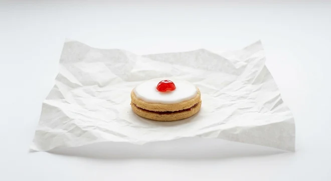 Greggs Empire Biscuit, iced jam-filled Empire biscuit with a jelly sweet on white paper, nutrition and calories