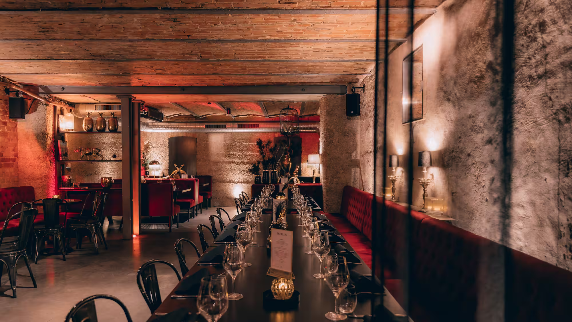 Gemütliches Restaurant mit langer Tafel, rot gepolsterten Bänken und gedämpfter Beleuchtung.