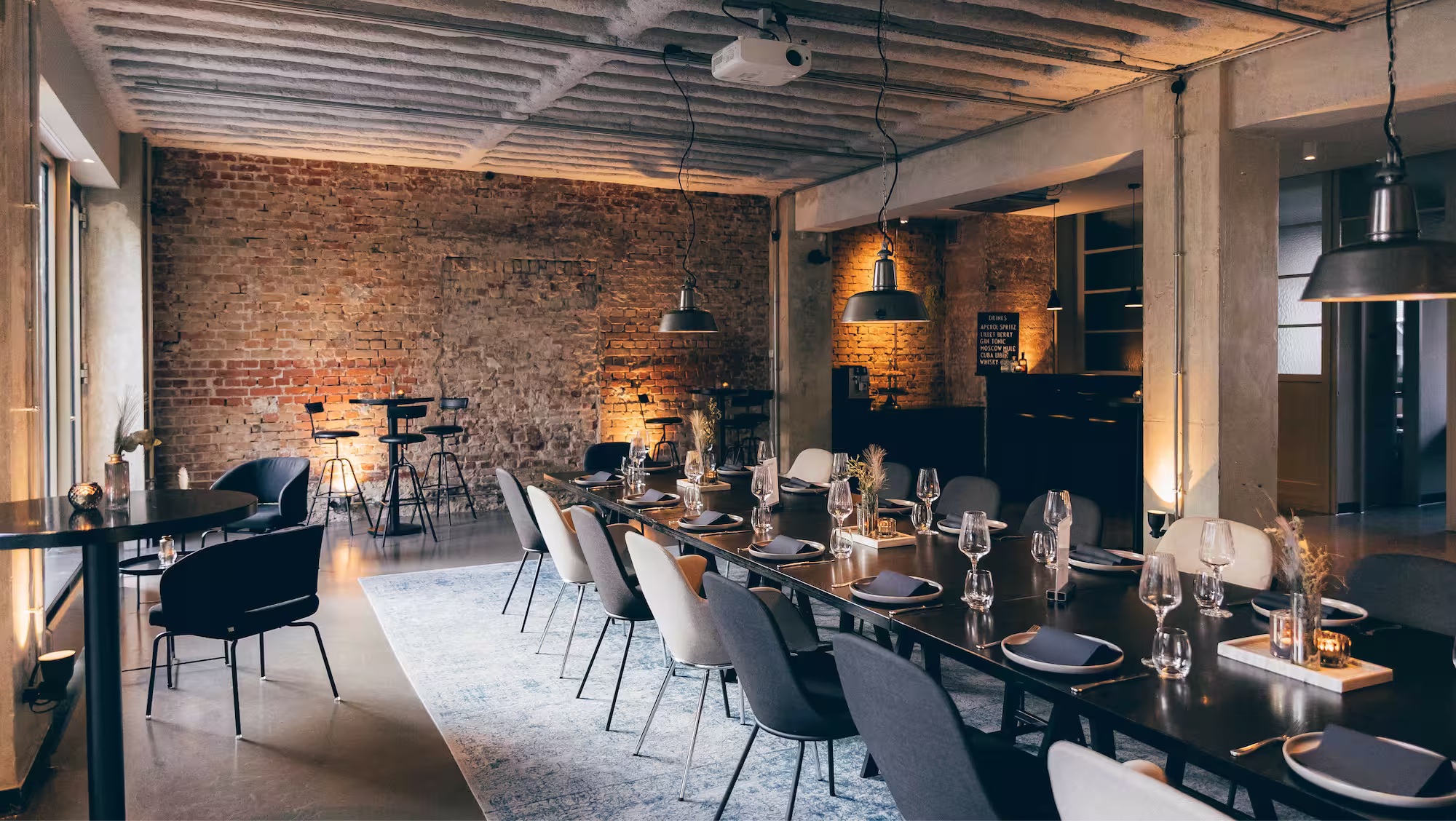 Modernes Esszimmer mit langem gedecktem Tisch, gemischten Stühlen, Ziegelwand und Industriebeleuchtung.