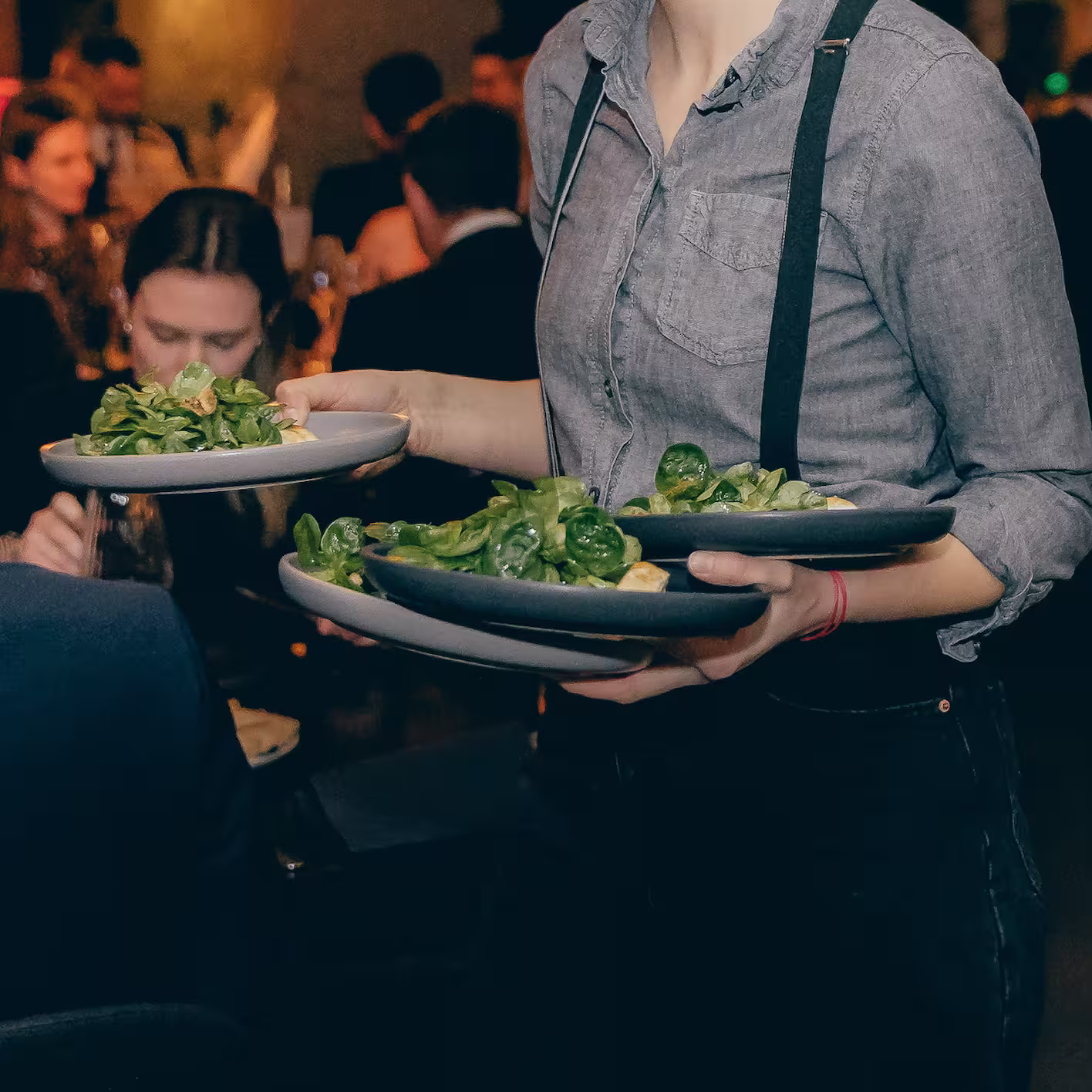 Kellner trägt mehrere Teller mit Salat in einem belebten Restaurant.
