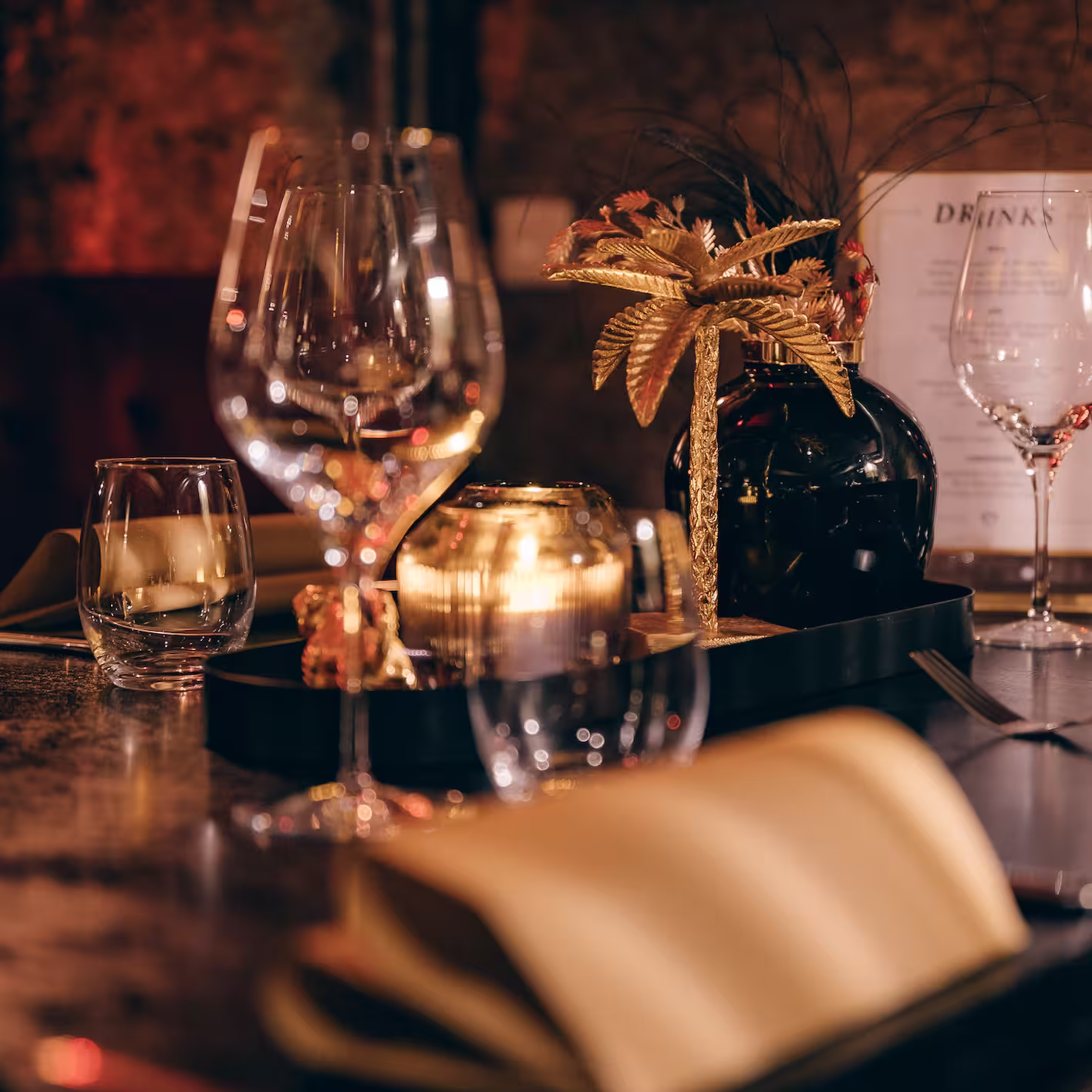 Stimmungsvoller gedeckter Tisch mit Weingläsern, Kerze und dekorativer goldener Palme.