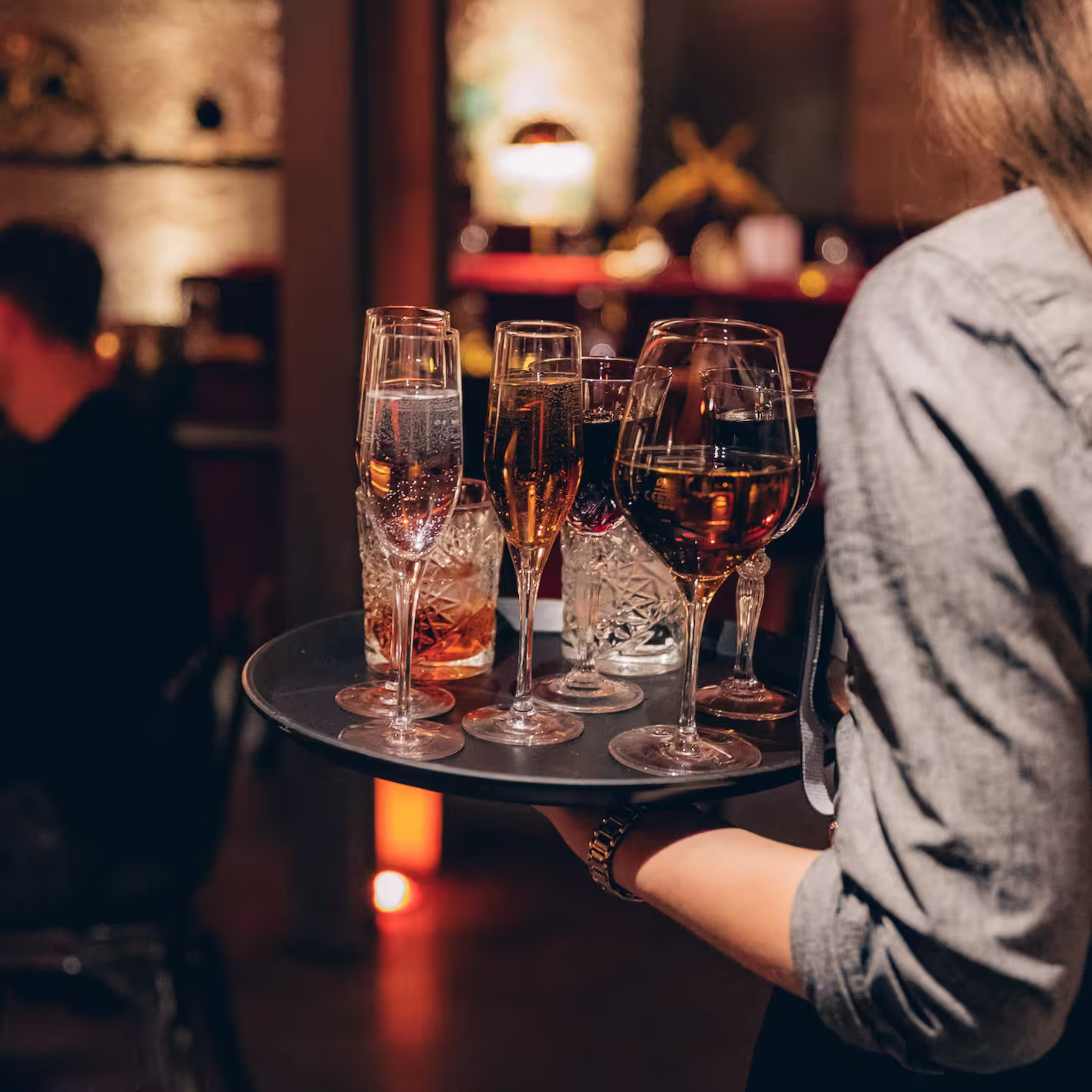 Eine Kellnerin trägt ein Tablett mit verschiedenen gefüllten Weingläsern und Getränken in einer Bar.