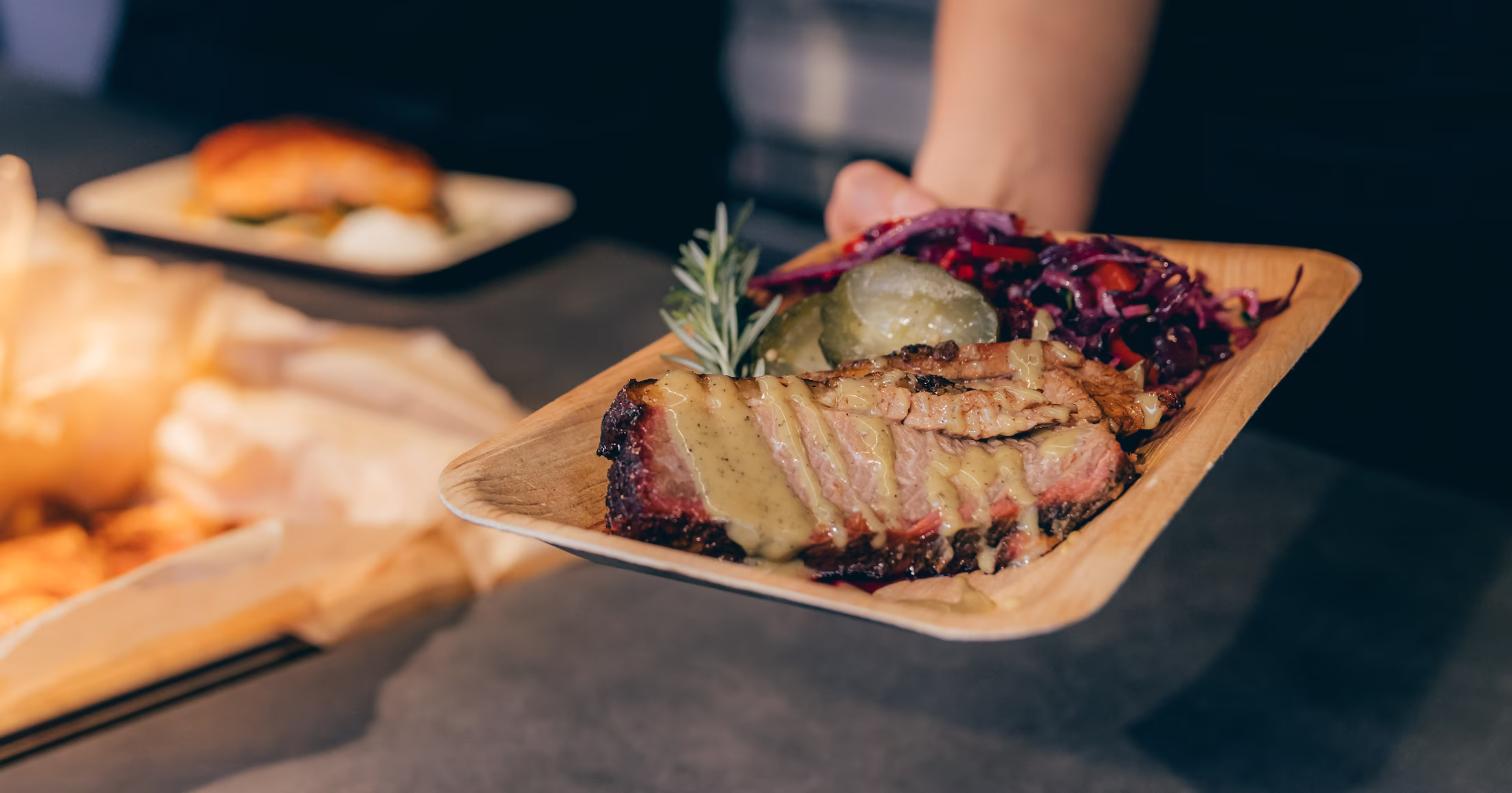Ein Teller mit BBQ-Rippchen, Senfsauce, roten Krautsalat, Gewürzgurken und einem Rosmarinzweig.