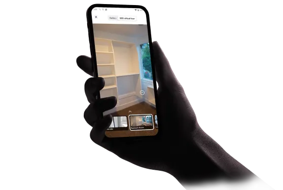 Hand holding a smartphone displaying a virtual tour of a room with built-in shelves and a window.