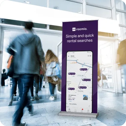Banner displaying an app called Reemio with the text 'Simple and quick rental searches' standing in a busy indoor area with blurred people walking by.