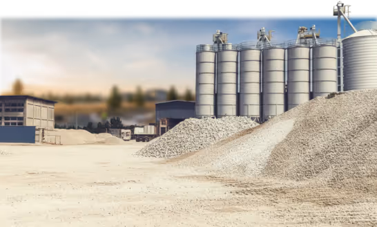 Industrial site with large gravel piles and tall silos under a clear sky.