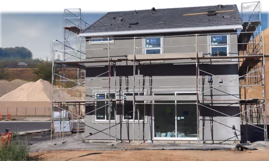 Two-story house under construction with scaffolding on front and large windows installed.