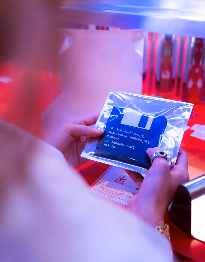 Person holding a sealed plastic package with a blue floppy disk and handwritten Italian text.