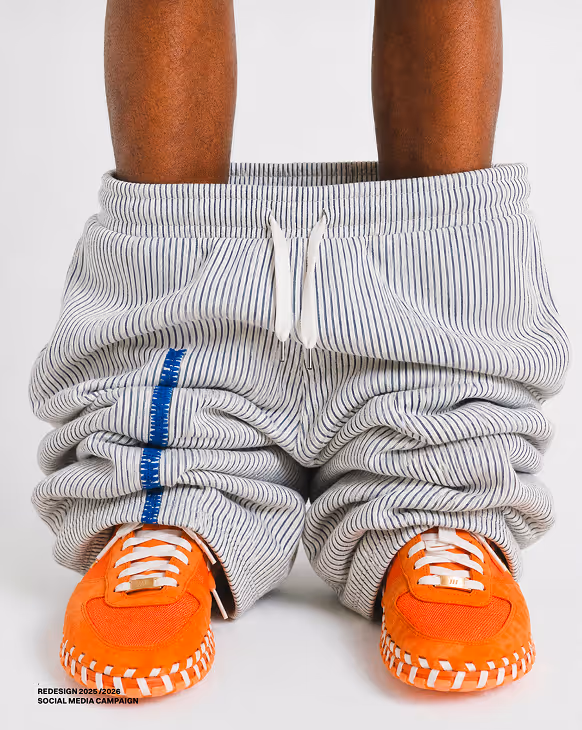 Person with pants pulled down around ankles wearing bright orange sneakers with white laces.