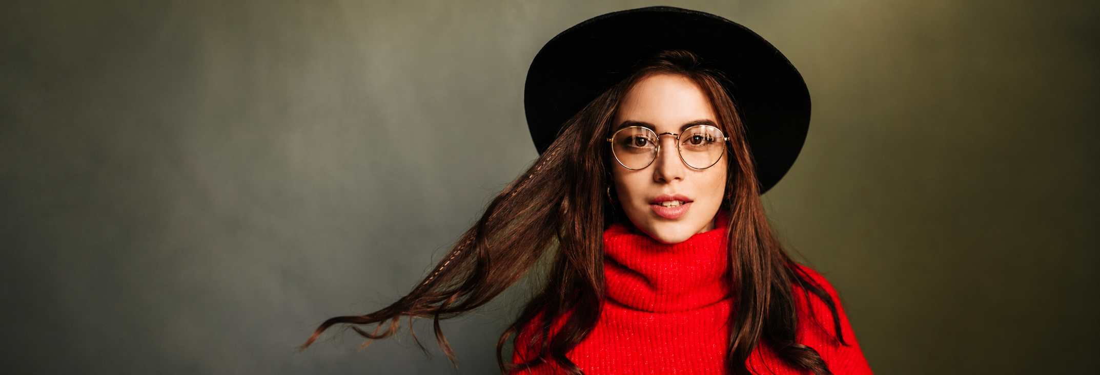 Woman with long brown hair wearing round glasses, a black hat, and a red turtleneck sweater.