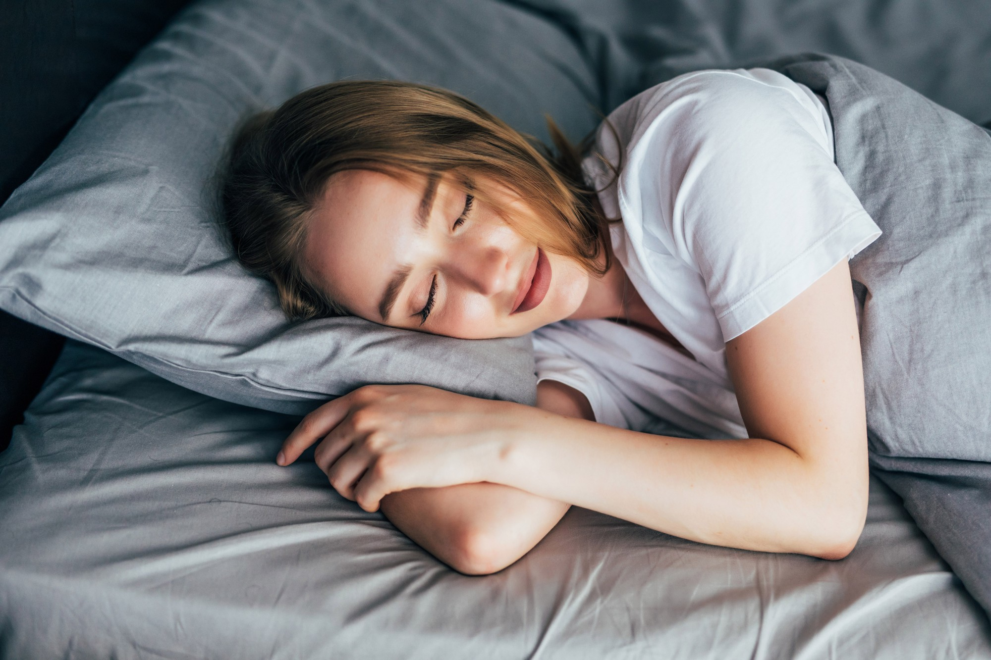 Woman peacefully sleeping on a gray pillow and bed with a white t-shirt.
