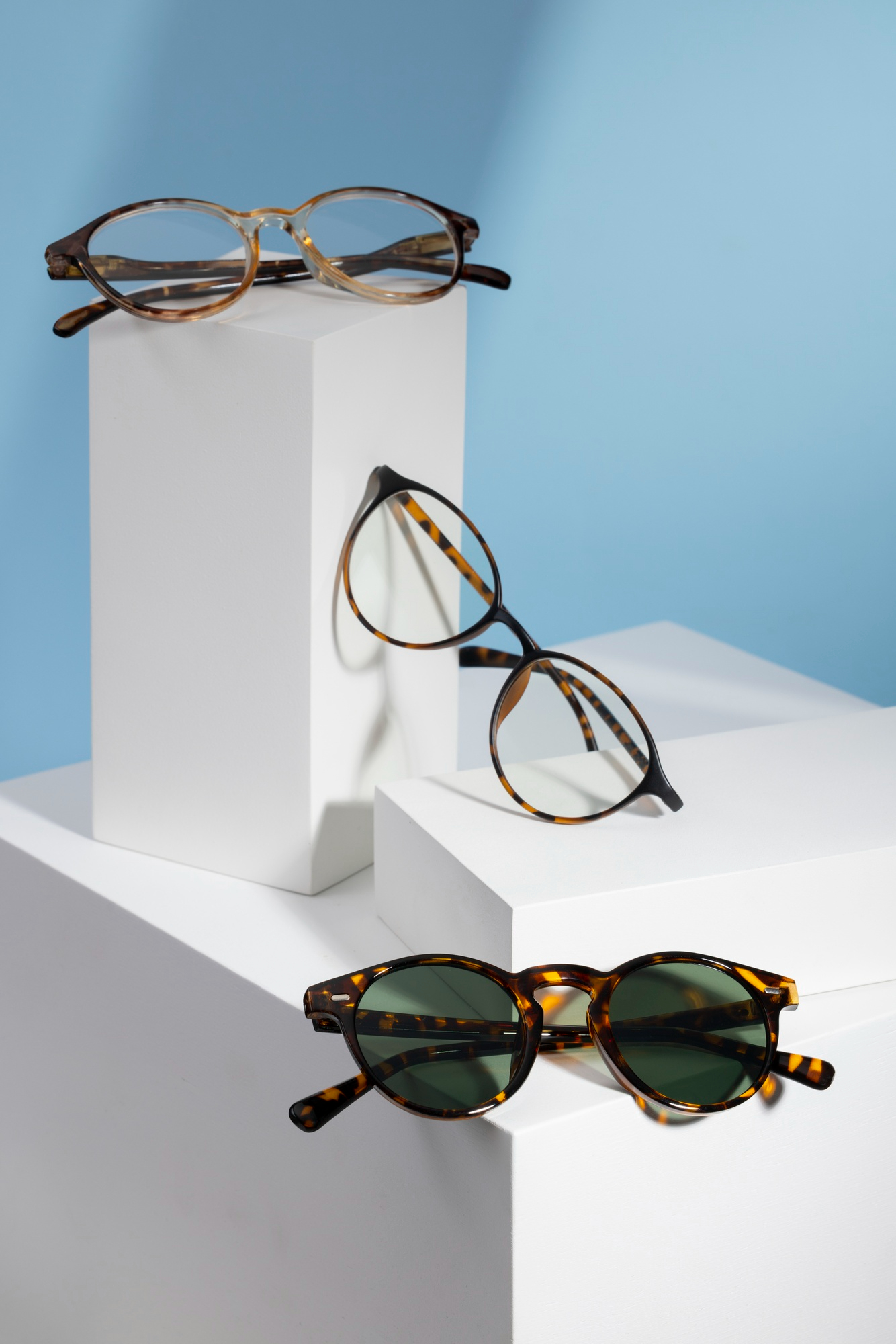Three pairs of tortoiseshell glasses displayed on white geometric stands against a blue background.