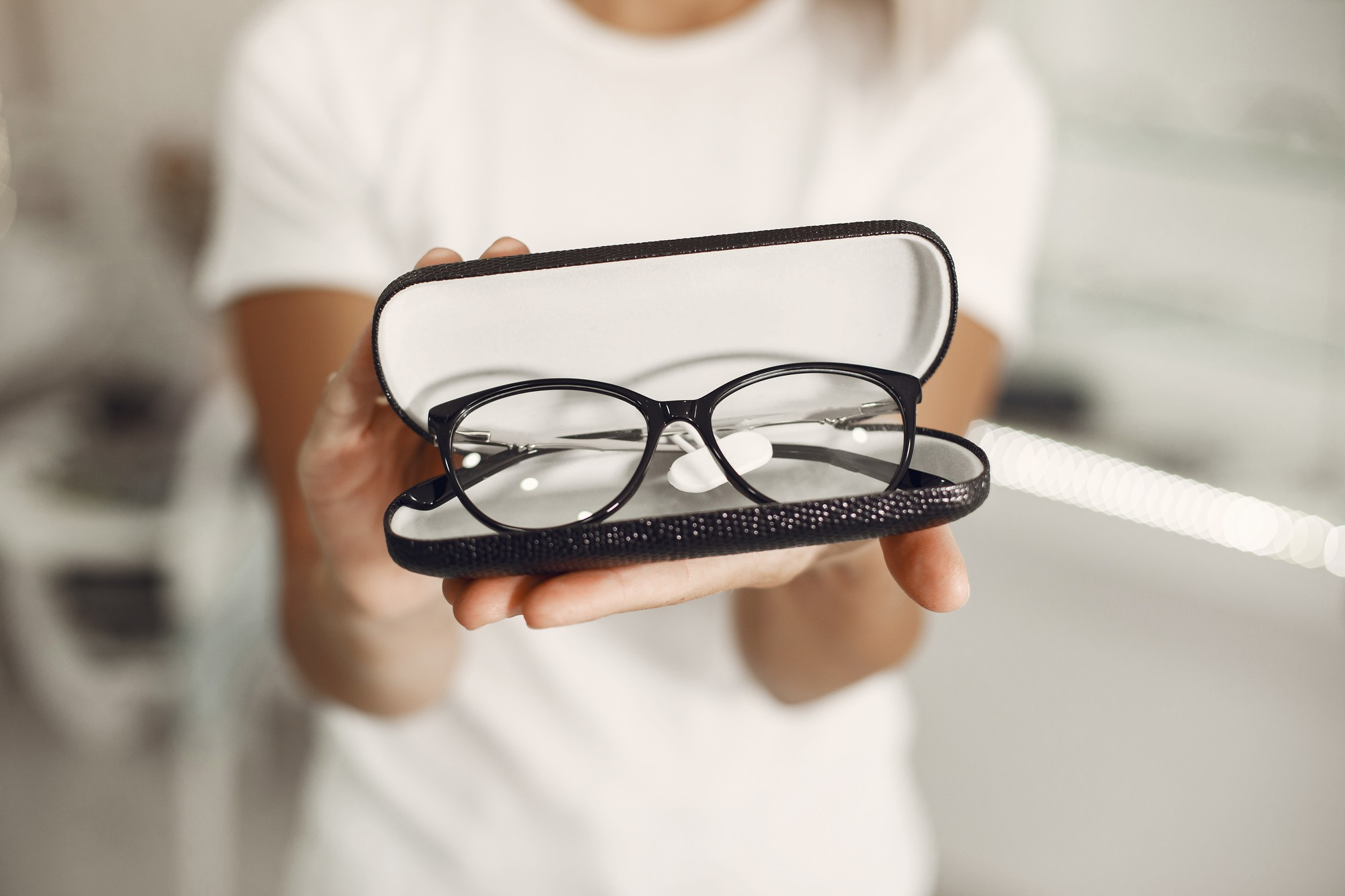 Person holding open glasses case with black framed eyeglasses inside.