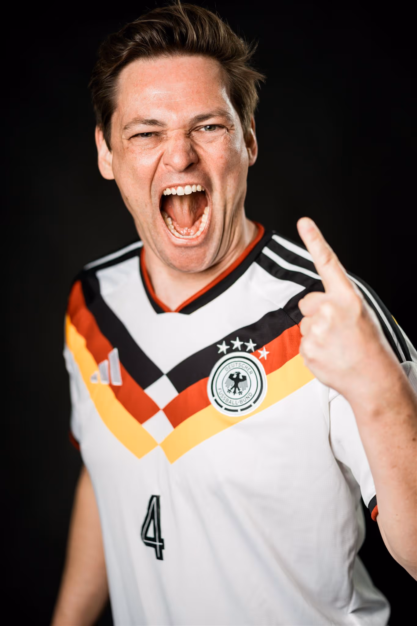Tino Hillemeyer in weißem deutschem Fußballtrikot mit aufgestelltem Finger und offenem Mund, als würde er jubeln oder anfeuern.