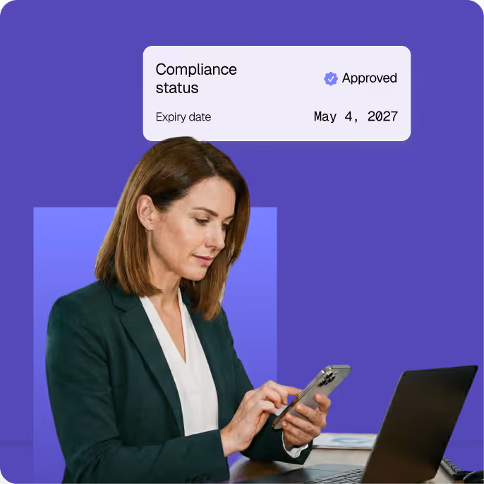 Woman in business attire using a smartphone at a desk with a laptop, with a digital overlay showing approved compliance status expiring May 4, 2027.