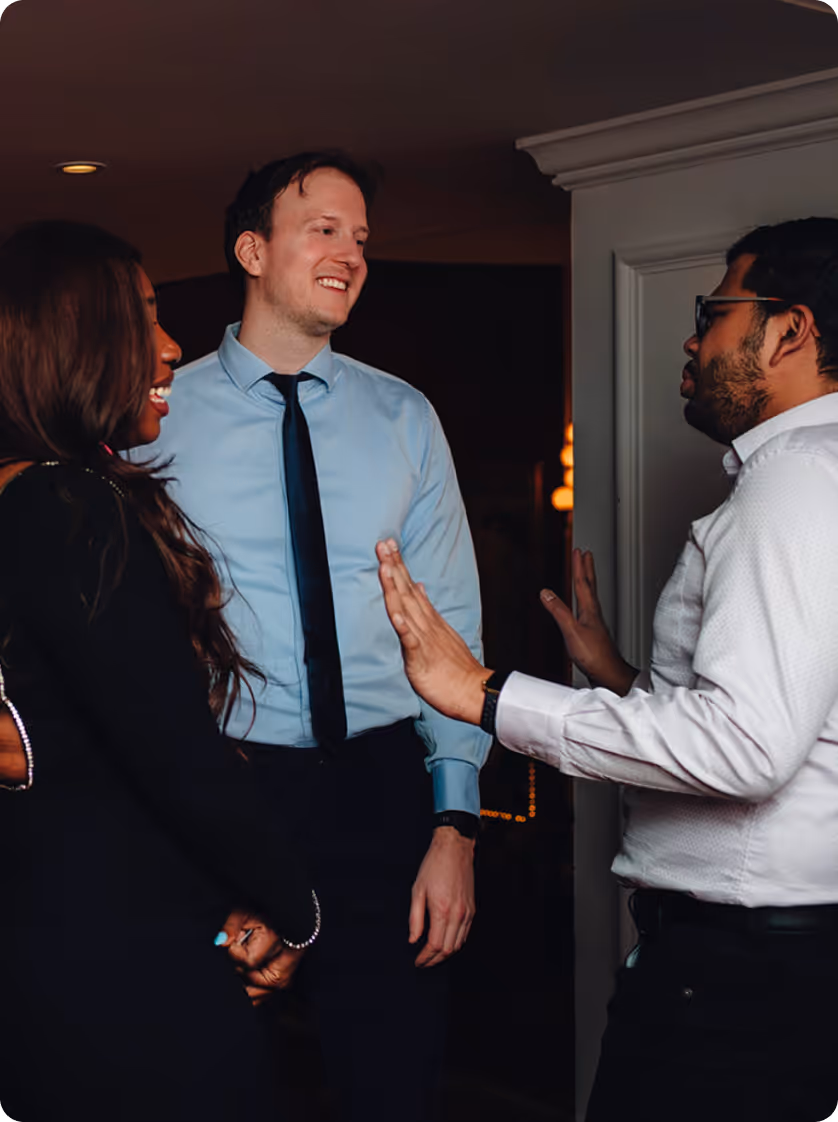 Trois personnes en tenue de cérémonie ont engagé une conversation à l'intérieur, un homme faisant des gestes des deux mains.