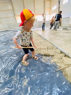 Ein Kinde mit Kappe ist zu erkennen mit einer kleinen Schaufel in der Hand auf der Baustelle.