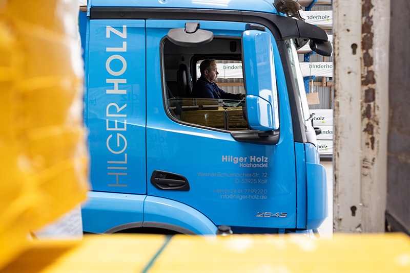 Ausschnitt von einem LKW Fahrer in blauem Mercedes LKW beladen mit Holz.