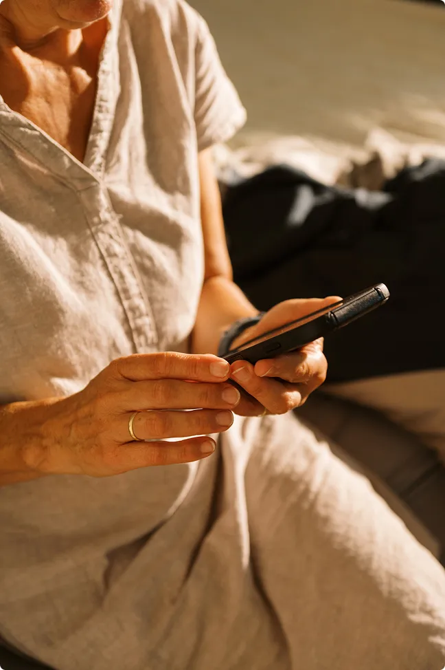 Person in light beige dress using a smartphone while sitting indoors with natural sunlight.