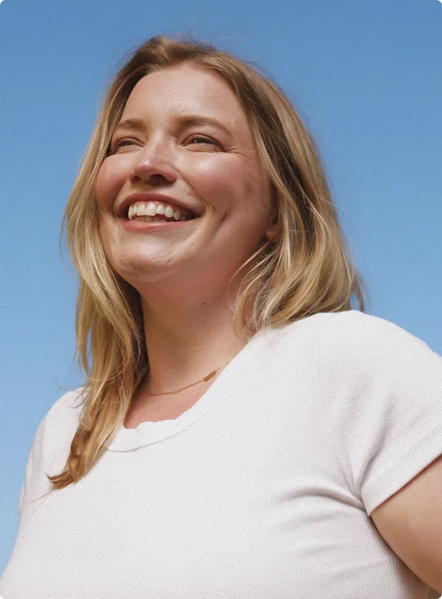 Smiling woman with blonde hair wearing a white shirt against a clear blue sky.
